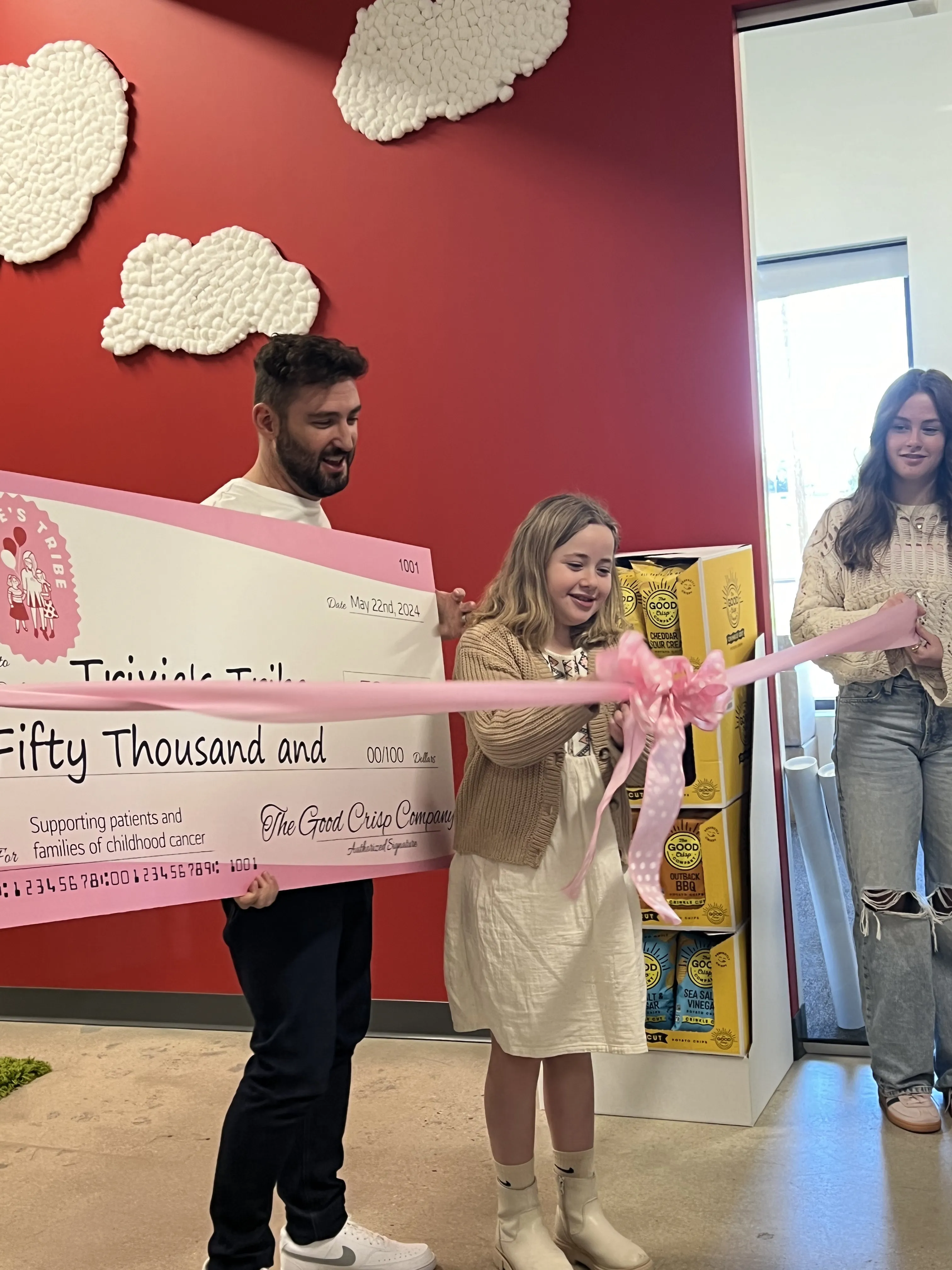Young girl cutting a pink ribbon in front of a giant cheque for fifty thousand dollars from The Good Crisp Company