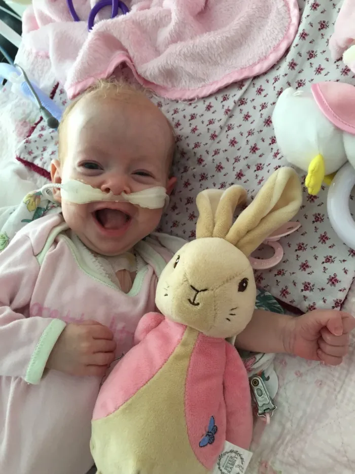 Baby Trixie laughing in her cot, cuddling a plush rabbit